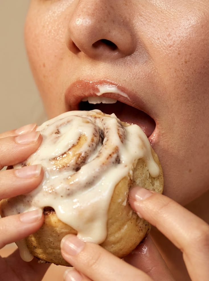 Pessoa mordendo um pão doce com cobertura, simbolizando alimentação emocional